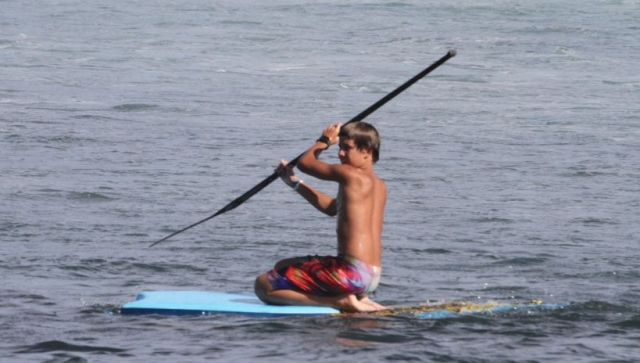 nino en una tabla de rodillas y con un remo en las manos